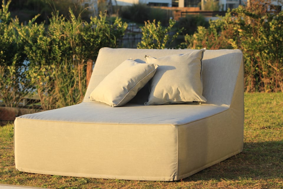 Camastro claro de exterior con almohadones a juego en un jardín al atardecer