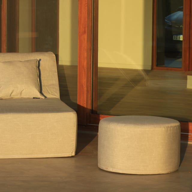 Puff circular de exterior tapizado en gris en un ambiente lounge de la colección Náutica de Velenza